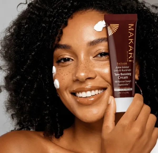 Makari Tone Boosting Cream tube held by a smiling woman