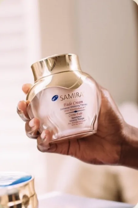 Hand holding a Samira Fade Cream jar with gold lid